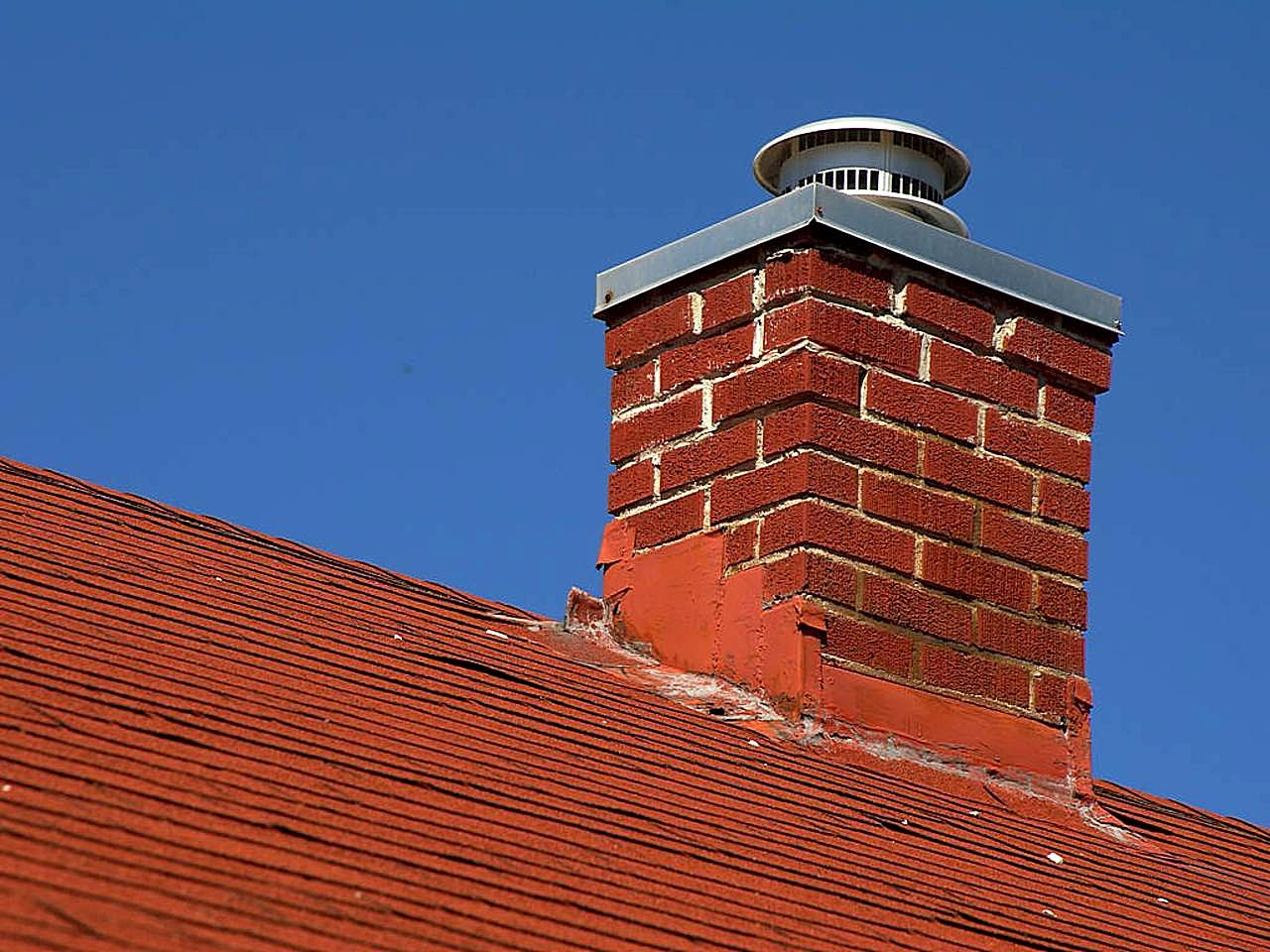 Red brick residential chimney with a metal chimney cap